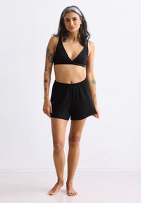 Zwarte bralette met een diepe V-hals, gecombineerd met zwarte shorts met een elastische taille. De stof is glad, heeft een effen kleur en geen zichtbare patronen.