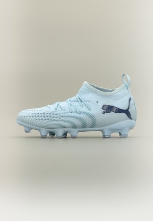 Ανοιχτό μπλε ποδοσφαιρικό παπούτσι με πλεκτό άνω μέρος, κορδόνια, θηλιά για τραβήγμα, υφή στην σόλα και σκούρο λογότυπο Puma στη φτέρνα, σε ουδέτερο φόντο.