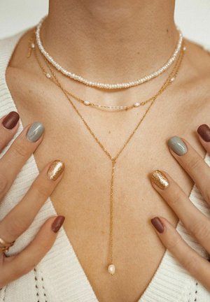 Layered necklaces with gold chains, white pearls, and a drop pendant. The neckline is highlighted with delicate designs and varied textures.