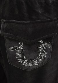 Schwarzer Samtstoff mit einer strukturierten Tasche. Die Tasche ist mit dekorativen Strasssteinen versehen, die in einem geschwungenen Muster angeordnet sind.