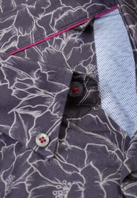 Herenoverhemd met een donker bloemenpatroon met witte contouren. De binnenkant van de kraag is blauw en wit gestippeld, met contrasterende roze accenten en knopen.