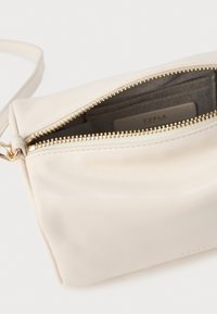 Krēmkrāsas ādas crossbody soma ar zelta metāla rāvējslēdzēju, plašu iekšpusi un gludu tekstūru. Iekļauj vienu siksnu ērtai nēsāšanai.
