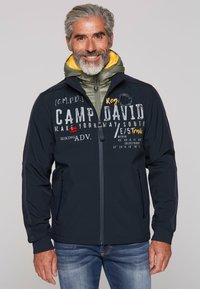 Marinejacke mit grüner Kapuze, frontzipp und Taschen. Verfügt über bedruckten Text und Designs in verschiedenen Farben. Lässige Passform, weiche Textur.