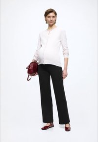 Hellrosa Cardigan mit Knöpfen, kombiniert mit schwarzen weit geschnittenen Hosen. Das Modell hält eine bordeauxrote Handtasche und trägt rote Ballerinas. Glatte Texturen sind sichtbar.