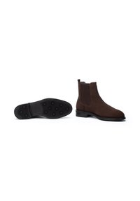 Bottines Chelsea en daim marron avec panneaux élastiques sur les côtés, semelle plate en caoutchouc et tirette. Texture lisse et forme effilée pour un design élégant.