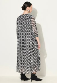 Robe longue à motif géométrique noir et blanc avec des manches transparentes trois-quarts, une silhouette fluide et une coupe à la cheville, assortie à des chaussures noires.