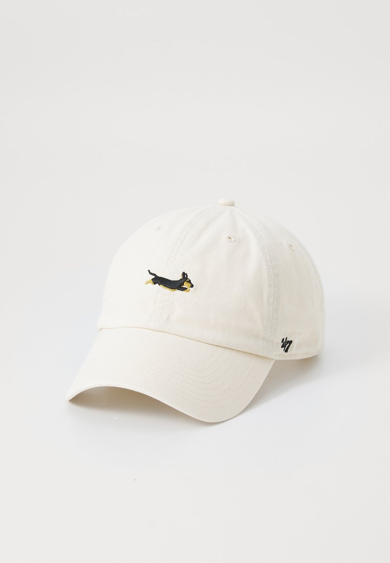 Boné de algodão creme com aba curva, apresentando um pequeno design de cachorro bordado em preto e amarelo na frente e um logotipo na lateral.