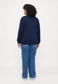 Navy blue sweatshirt with long sleeves and a round neckline, paired with light blue wide-leg jeans and gray sneakers.