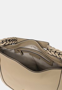 Borsa a tracolla in pelle beige con manico intrecciato, ampia tasca interna, tasca con zip e rifiniture nere a contrasto lungo i bordi.