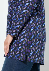 Musta yläosa, jossa on värikäs kuvio sateenvarjoista, palloista ja kiehkuroista. Pitkät hihat ja sivuaukot. Yhdistetty tummansinisiin farkkuihin.