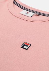 T-shirt rose pâle à col rond avec un petit logo Fila brodé en rouge, bleu marine et blanc centré sous l'encolure.