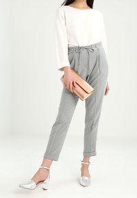 Szare, dopasowane spodnie z talią na sznurek, zestawione z białą bluzką z dekoltem w kształcie łódki. Trzyma metaliczną złotą kopertówkę; ma na sobie srebrne buty na obcasie.