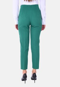 Pantaloni verdi su misura con una vestibilità slim, caratterizzati da una texture liscia e dettagli delle cuciture. Abbinati a tacchi alti neri, mostrati da dietro.