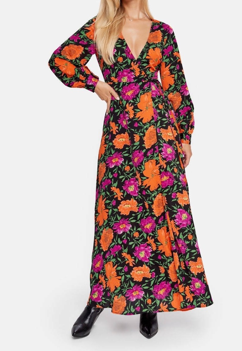 Robe maxi en tissu noir ornée de motifs floraux vibrants en orange et violet, décolleté en V profond, manches longues et silhouette fluide.
