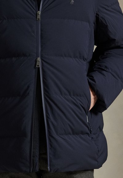 Tamsiai mėlyna pūsta striukė su užtrauktuku priekyje, elastinėmis rankogaliais ir šoninėmis kišenėmis. Lygios tekstūros su pūstiniu raštu ir subtiliu logotipo akcentu.