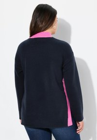 Pull color block marine et rose, avec un col côtelé rose et des panneaux latéraux roses. Texture douce, coupe décontractée et ourlet au dos plus long.