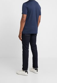 T-shirt navy a maniche corte, in morbido misto cotone, con taglio dritto. Indossato con jeans blu scuro e sneakers bianche con dettagli neri.