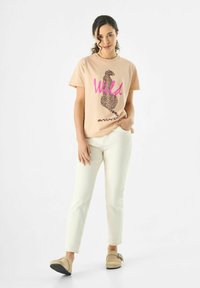 T-shirt en coton rose clair avec un imprimé léopard marron et le mot "Wild" en rose vif, assorti à un pantalon blanc et des chaussures slip-on beiges.