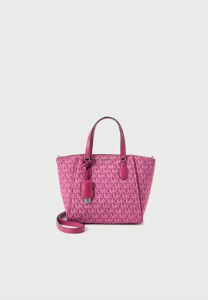 Różowa torba typu tote marki Michael Kors z monogramem, podwójnymi uchwytami, przymocowaną zawieszką i odpinanym paskiem na ramię na białym tle.