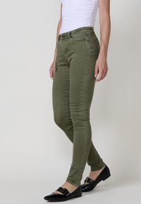 Olivové skinny džíny s předními kapsami, dekorativním švem a vybledlou texturou. Kombinované s černými balerínami s kovovými přezkami.