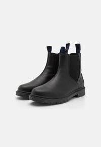 Botas Chelsea negras con parte superior de piel lisa, paneles laterales elásticos y tiradores. Suela de goma resistente con dibujo texturizado para mayor agarre.