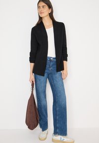 Czarny prążkowany kardigan, biały T-shirt, niebieskie szerokie dżinsy oraz brązowa zamszowa torba. Sneakersy z beżowymi i jasnoniebieskimi akcentami.