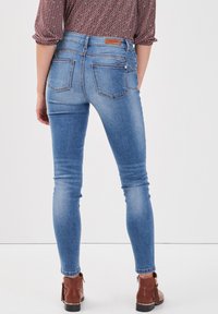 Jeans ajustados de color azul con un lavado desgastado, cinco bolsillos y costuras visibles. Combinados con botas marrones hasta el tobillo con un acabado de cuero texturizado.