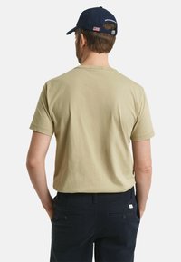 Beige bomull t-shirt med rund hals och korta ärmar, sedd bakifrån, matchad med mörkblå byxor med bakfickor.