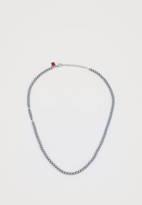Blå pärlhalsband med en silverkedja. Har en metallisk lås med en röd etikett och en slät, rundad textur.