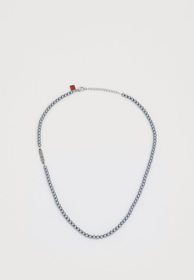 Blå pärlhalsband med en silverkedja. Har en metallisk lås med en röd etikett och en slät, rundad textur.