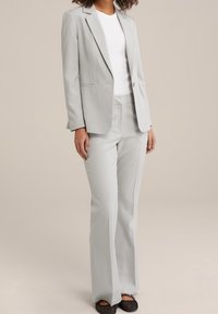 Light grey tailored suit with a fitted blazer and flared trousers, paired with a white t-shirt, featuring a subtle texture and classic design.
