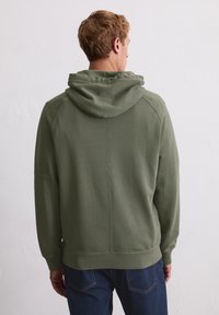 Sweatshirt à capuche vert olive avec une coupe décontractée, en tissu texturé, et des bords côtes aux poignets et à l'ourlet. Présente une capuche structurée et des détails de couture au dos.