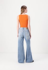 Oransje ribbet tanktop med rund halsringning, kombinert med lyseblå vide jeans med baklommer og midjehøyde.