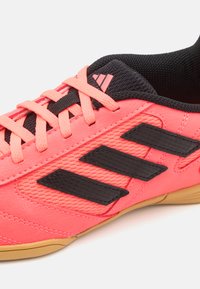 Zapatilla deportiva rosa y negra con parte superior texturizada, que presenta el logotipo de tres franjas en negro, lengüeta de malla y suela de goma.
