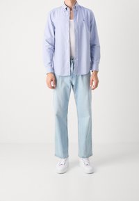 Lichtblauw overhemd met knopen, wit hemd eronder, lichtblauwe jeans en witte sneakers. Casual pasvorm met klassieke designelementen.