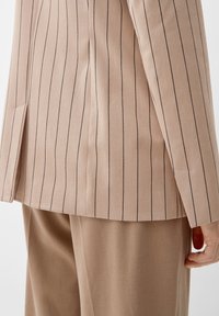 Giacca da abito beige a righe in tessuto testurizzato, con un taglio dritto, un solo spacco e una vestibilità sartoriale.