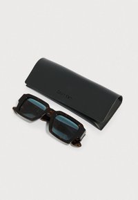 Sončna očala z raščeno školjko in temnimi lečami, s robustno pravokotno obliko. Vključuje eleganten črni etui z odtisnjenim napisom "Calvin Klein".