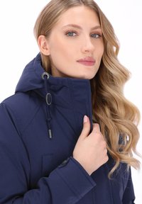 Granatowa kurtka z kapturem, z zamknięciem na sznurek, kieszenią na zamek i mankietami na guziki. Gładka faktura i dopasowany krój.