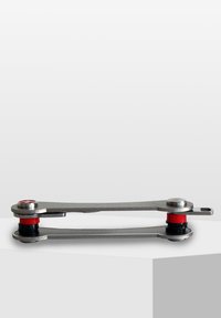 Kompakt multitool i rostfritt stål med röda och svarta accentringar, med en smal, avlång design och två cirkulära fästdon.