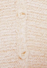 Knit krēmkrāsas kardigāns ar teksturētu rakstu un apaļu, četru caurumu pogu priekšējā aizdare.