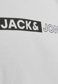 Witte T-shirt met een zwarte grafische print met de tekst "JACK & JONES" in vetgedrukte, sans-serif lettertype. Zachte katoenstructuur.