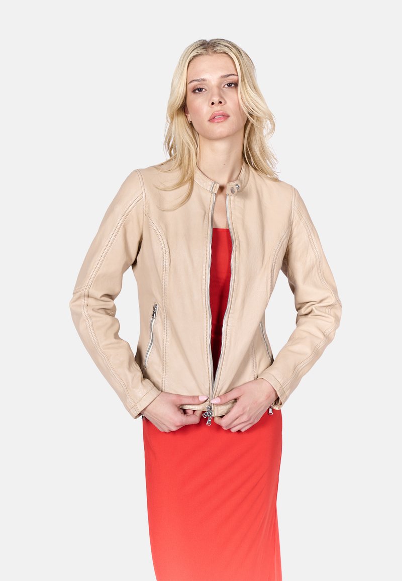 Beige Lederjacke mit Rundhalsausschnitt, Reißverschlussfront und zwei seitlichen Reißverschlusstaschen. Getragen über einem roten Kleid, das dezente Nähtdetails aufweist.