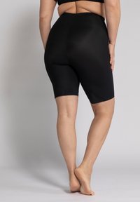 Shorts neri a vita alta in un tessuto elastico e liscio; lunghezza a metà coscia con una silhouette aderente. Nessun motivo o hardware visibile.