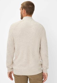 Beige Rippstrickpullover mit einem Stehkragen und langen Ärmeln, der eine strukturierte Oberfläche aufweist. Die Rückansicht zeigt die Nahtdetails und die lockere Passform.