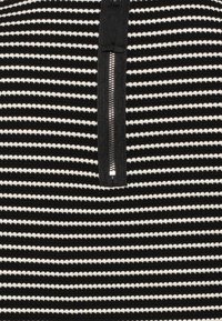 Indumento a strisce bianche e nere con chiusura frontale a metà zip. Tessuto testurizzato con strisce orizzontali, colori a contrasto e una zip liscia.