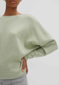 Maglione oversize di un verde chiaro con scollatura a barca ampia e maniche lunghe arricciate, realizzato in un morbido tessuto testurizzato.