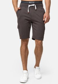 Grå cargo shorts med elastisk talje og snor. Har sidelommer og en afslappet pasform. Båret med hvide sneakers.