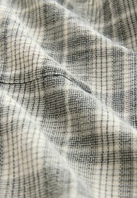 Woven fabric w kolorze jasnej kremowej z tłem i wzorem kratki w ciemnym niebieskim. Tekstura wydaje się miękka i lekko pomarszczona.