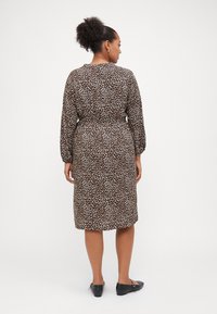 Robe à imprimé léopard avec des manches longues, taille cintrée et coupe mi-genoux. Fabriquée en tissu léger, avec une texture lisse. Escarpins noirs.