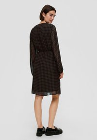 Zwart jurkje met lange mouwen en een geometrisch bruine print. Heeft een aansluitende taille en valt tot halverwege de kuit. Gekocht met zwarte platform schoenen.